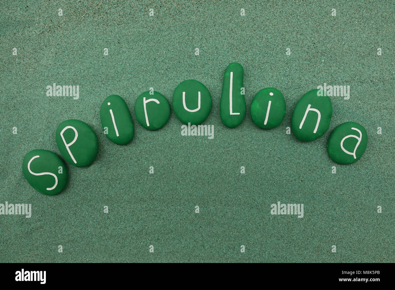 Spirulina Wort mit grün bemalten Steinen Zusammensetzung über grünen Sand Stockfoto