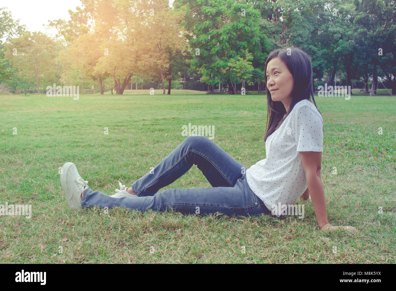 Schöne asiatische Frau Sitzen und Liegen auf der grünen Wiese im Park entspannen. Sie Gefühl Freude und Erfrischung. Stockfoto