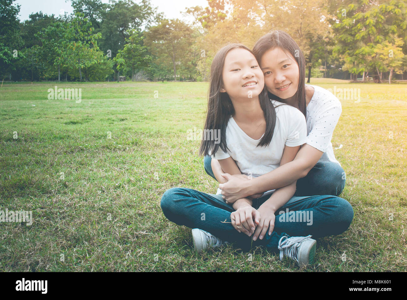 Adorable und Familie Konzept: Frau und Kind sitzen auf grünem Gras entspannen. Sie umarmen und Gefühl lächeln Glück in den Park im Vintage Style. Stockfoto