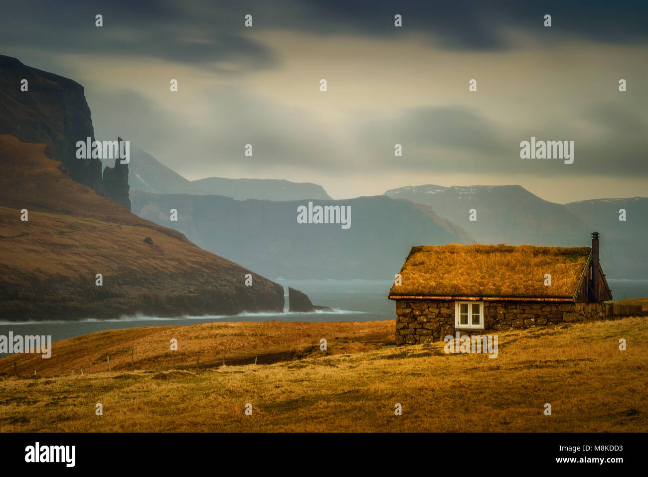 Einsame alte Kabine mit grasbewachsenen Dach und Hexe Finger Felsen im Hintergrund, Färöer Inseln Stockfoto