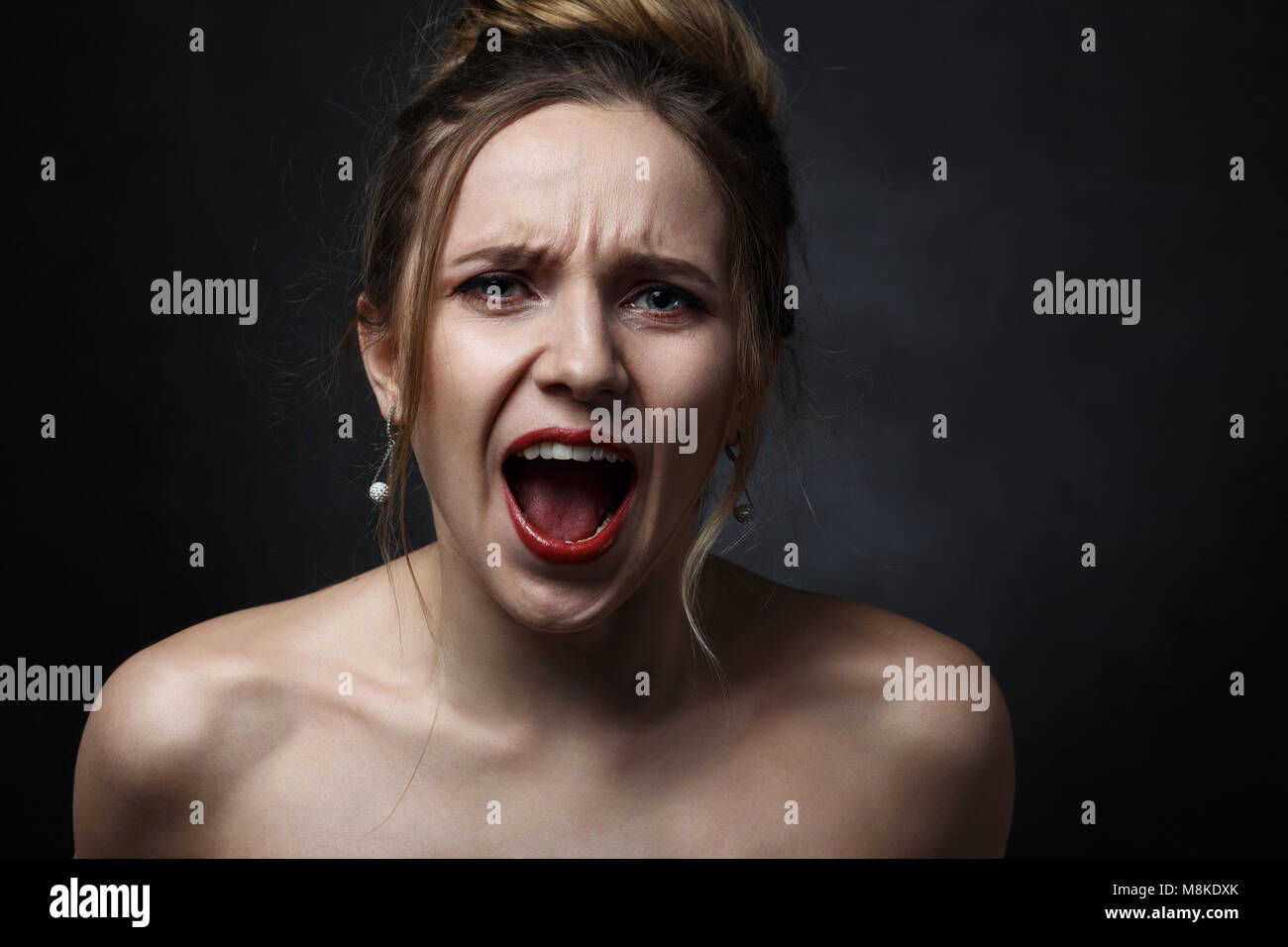 Junge wütende Frau auf schwarzem Hintergrund schreiend auf Kamera Stockfoto