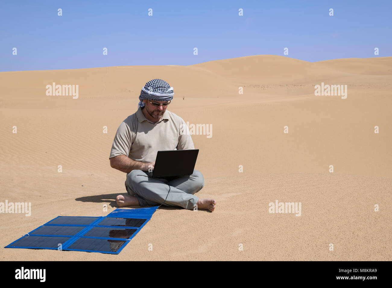 Ein Mann arbeitet ferngesteuert an einem Laptop neben einem tragbaren Sonnenkollektor in der Wüste, Selbstvertrauen und Nachhaltigkeit in einer ferngesteuerten Umgebung mit Kopierraum Stockfoto