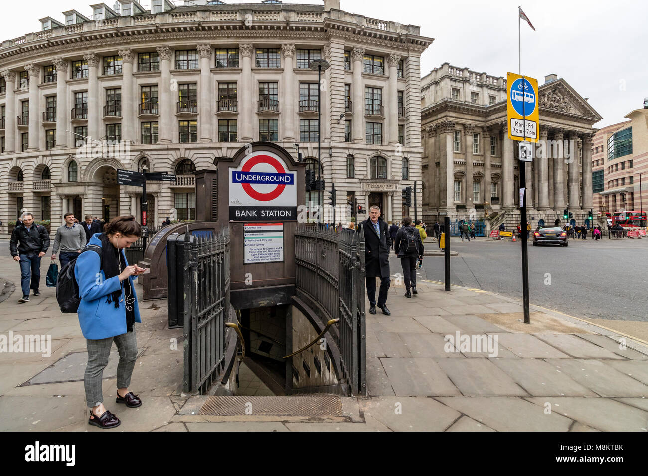 Eine Frau, die ihr Telefon außerhalb Bank Tube Station Eingang in der Londoner City prüfen Stockfoto
