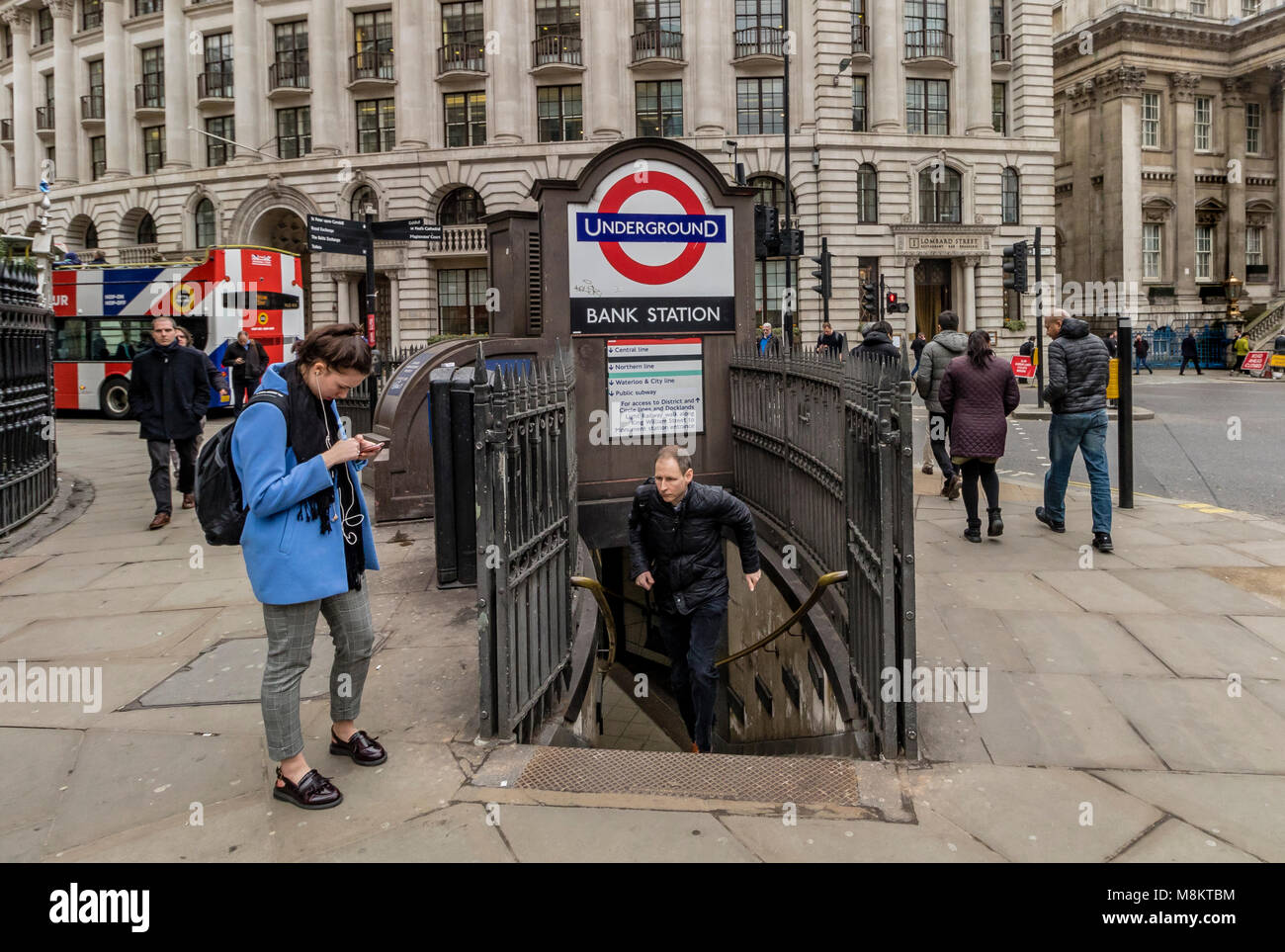 Eine Frau, die ihr Telefon außerhalb Bank Tube Station Eingang in der Londoner City als einen Mann hetzt die Schritte von der U-Bahnstation Eingang Stockfoto