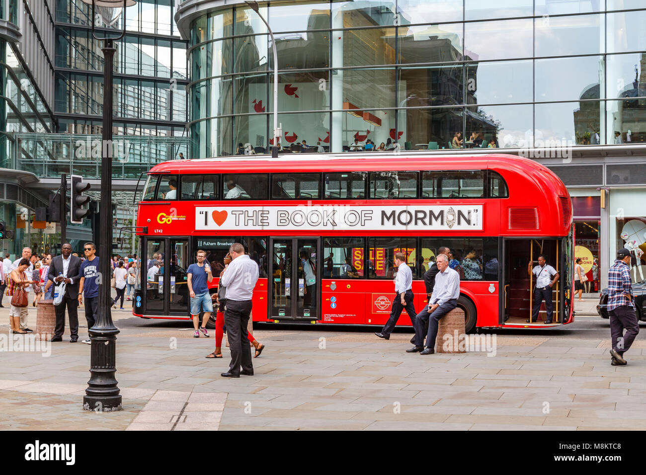 Mann, der an einem konkreten Poller an der Victoria Street, London sitzen, als Nr. 11 Bus fährt mit einer Werbung für das Buch der Morman auf der Seite Stockfoto