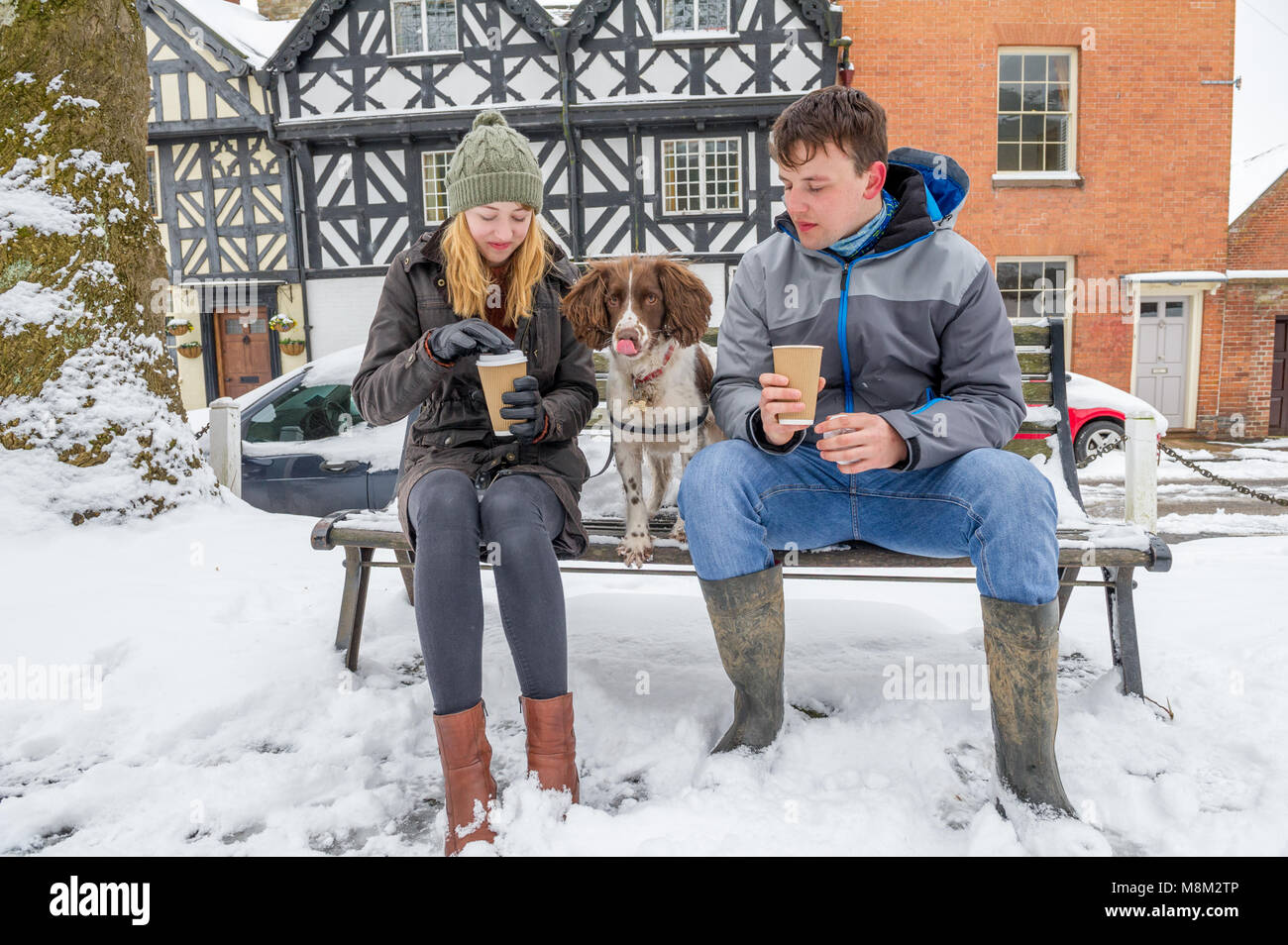Ludlow, Shropshire, England, UK. 18. März 2018. Junges Paar und ihrem Hund genießen ein heißes Getränk auf eine verschneite Bank in Ludlow, Shropshire nach dem über Nacht Schnee Sturm. Alan Beastall/Alamy leben Nachrichten Stockfoto