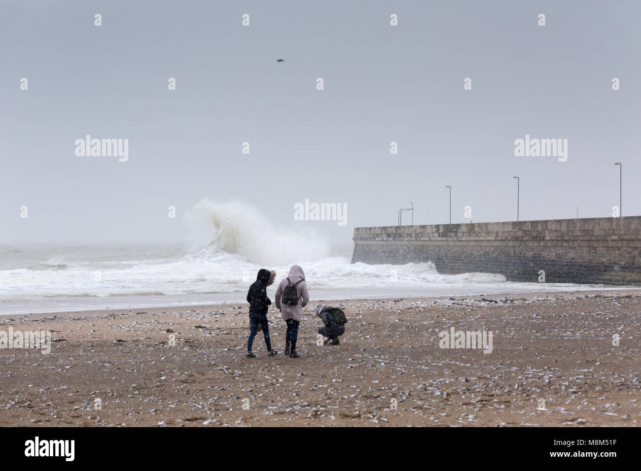 Ramsgate, Kent, Vereinigtes Königreich 18. März, 2018. Drei junge Leute am Strand während eines Schneesturms mit einer grossen Welle hinter Ihnen in der Nähe des Hafens. Sue Holness Credit: Sue Holness/Alamy leben Nachrichten Stockfoto