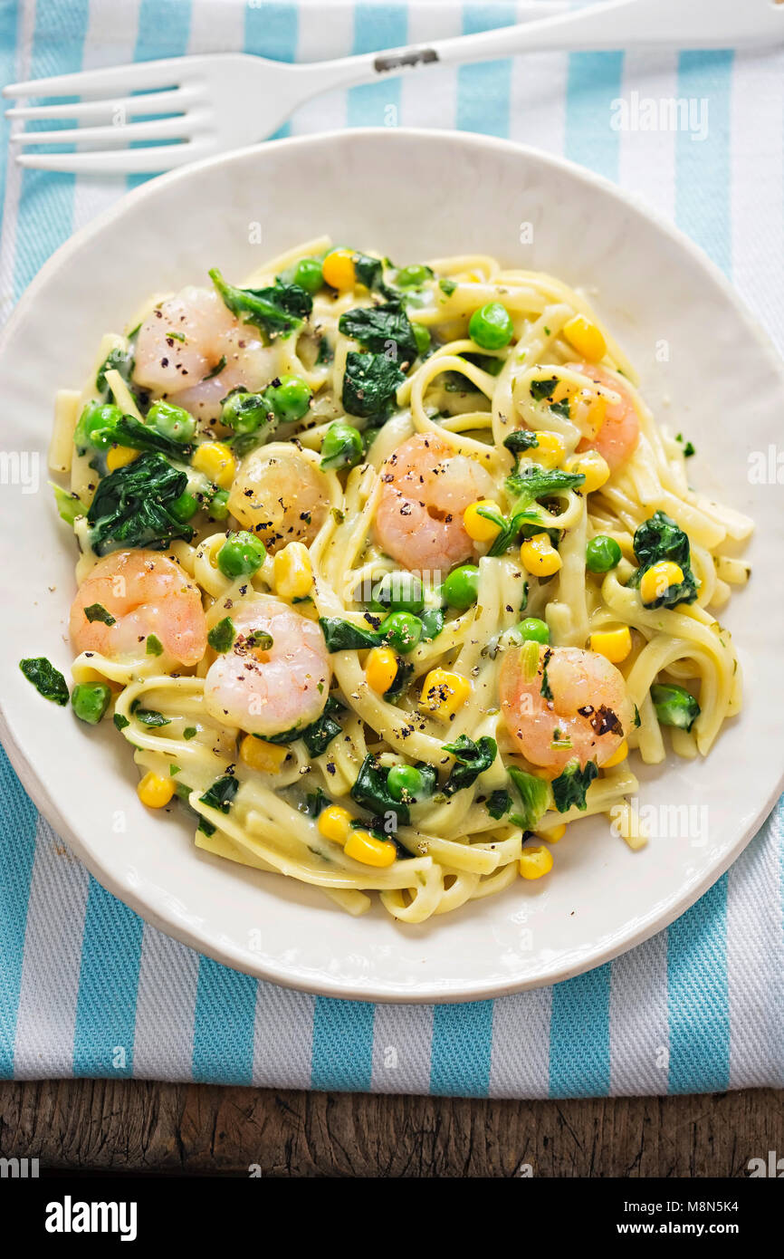 Cremige King Prawn Tagliatelle mit Erbsen, Spinat und Mais Stockfoto