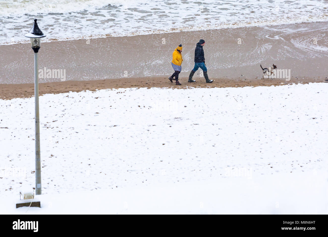 Paar mit Hund entlang der Küste mit Bournemouth Strand Meer in Schnee am Bournemouth, Dorset, England UK im März abgedeckt Stockfoto