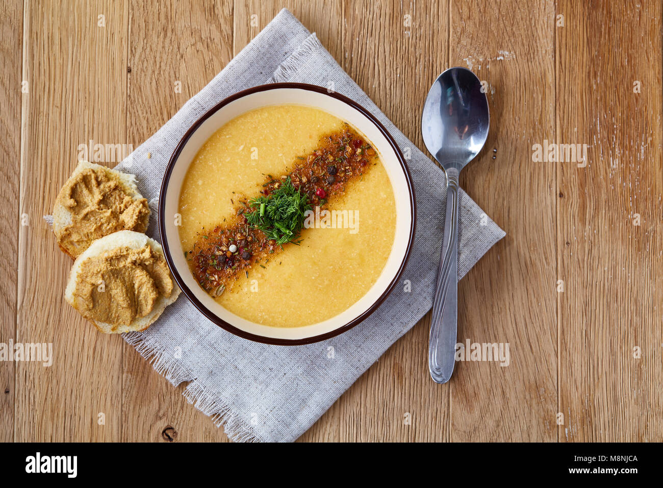 Lila Schale, cremige Kürbissuppe mit Dill garniert, serviert mit getoasteten Brotscheiben mit Paste auf homespun Serviette über rustikale Hintergrund, Stockfoto