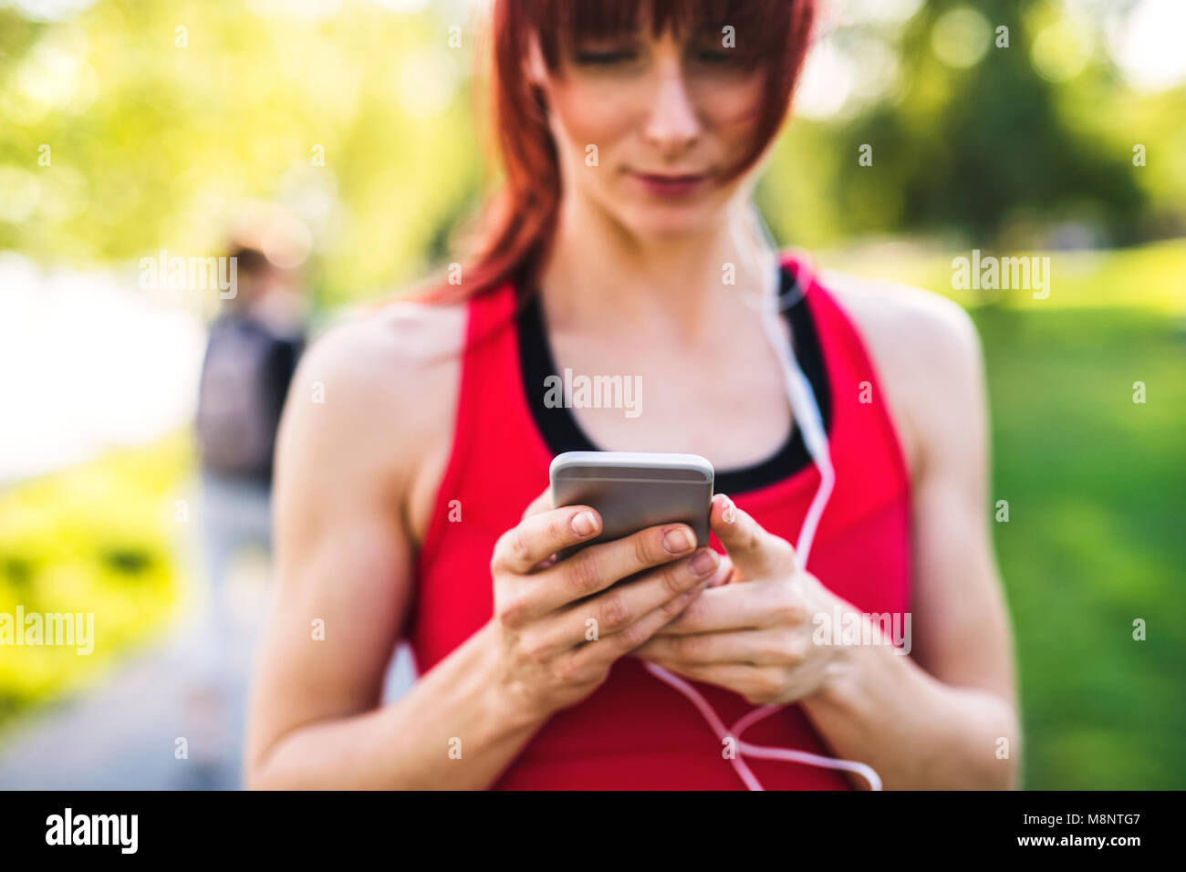 Junge Athlet im Park Holding smart phone, Musik hören. Stockfoto