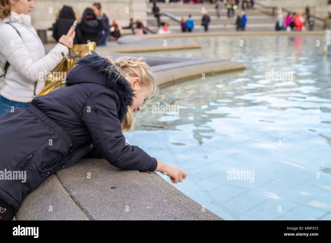 Blonde Kind, kleines Mädchen mit Zöpfen, Geflechte biegen in eine, Springbrunnen, werfen in Münzen, Trafalgar Square London, Großbritannien Stockfoto