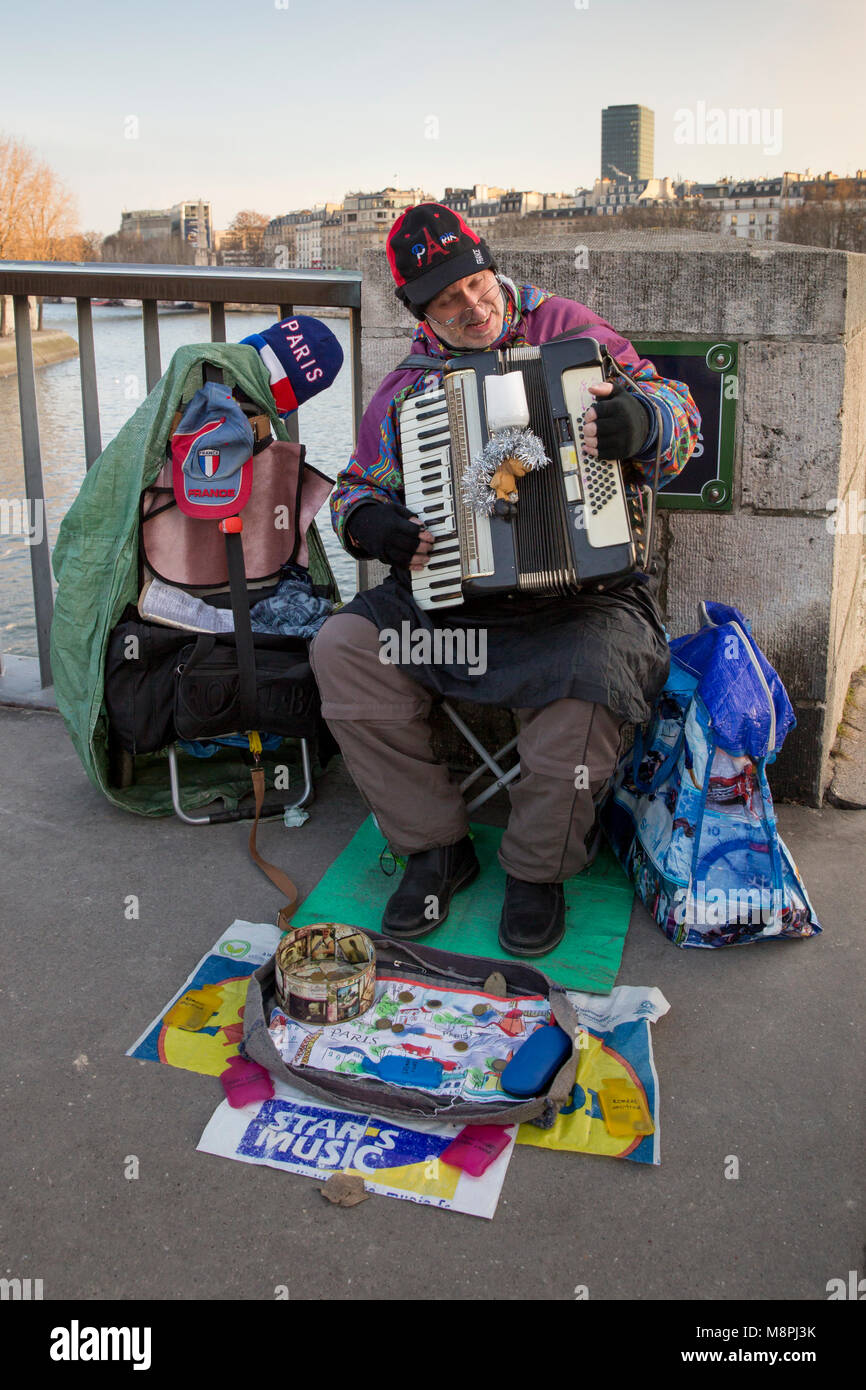 An einem kalten Wintertag ein Straßenmusiker spielen ein Akkordeon für Ersatzteile ändern auf Pont Saint Louis in Paris, Frankreich. Stockfoto