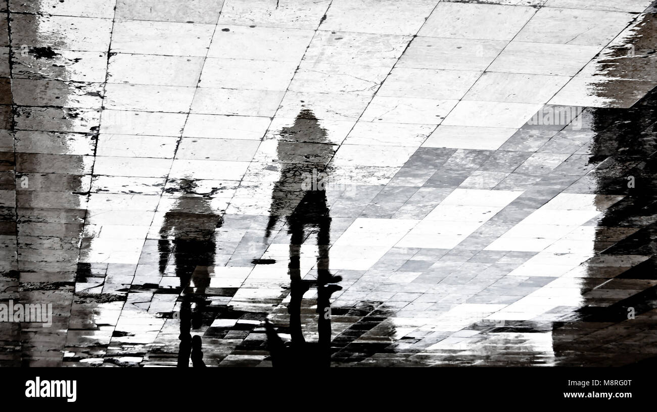 Unscharfe Reflexion Schatten Silhouette von zwei Menschen zu Fuß die Stadt Straße gemusterten Bürgersteig auf einem dunklen regnerischen Tag Stockfoto