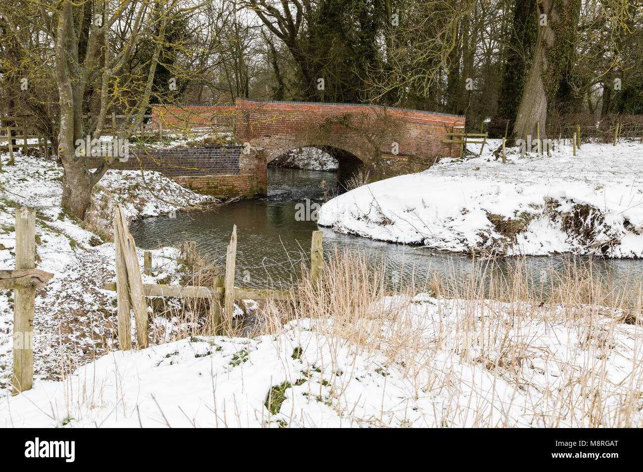 Eine verschneite Winterlandschaft des Flusses Sinn vorbei unter einer Straßenbrücke Schuß an Newton Harcourt, Leicestershire, England, UK. Stockfoto