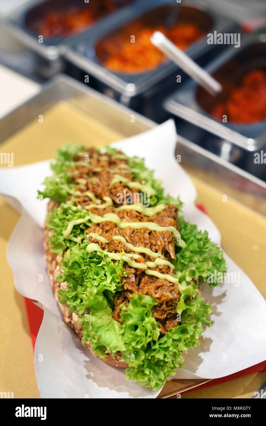 Köstliche zog pork Sandwich mit Geschredderten würzigen Fleisch beträufelt mit einem Dressing auf einem Bett von Salat auf das verfügbare Papier serviert in einem Fast Food Restaurant, Bar Stockfoto
