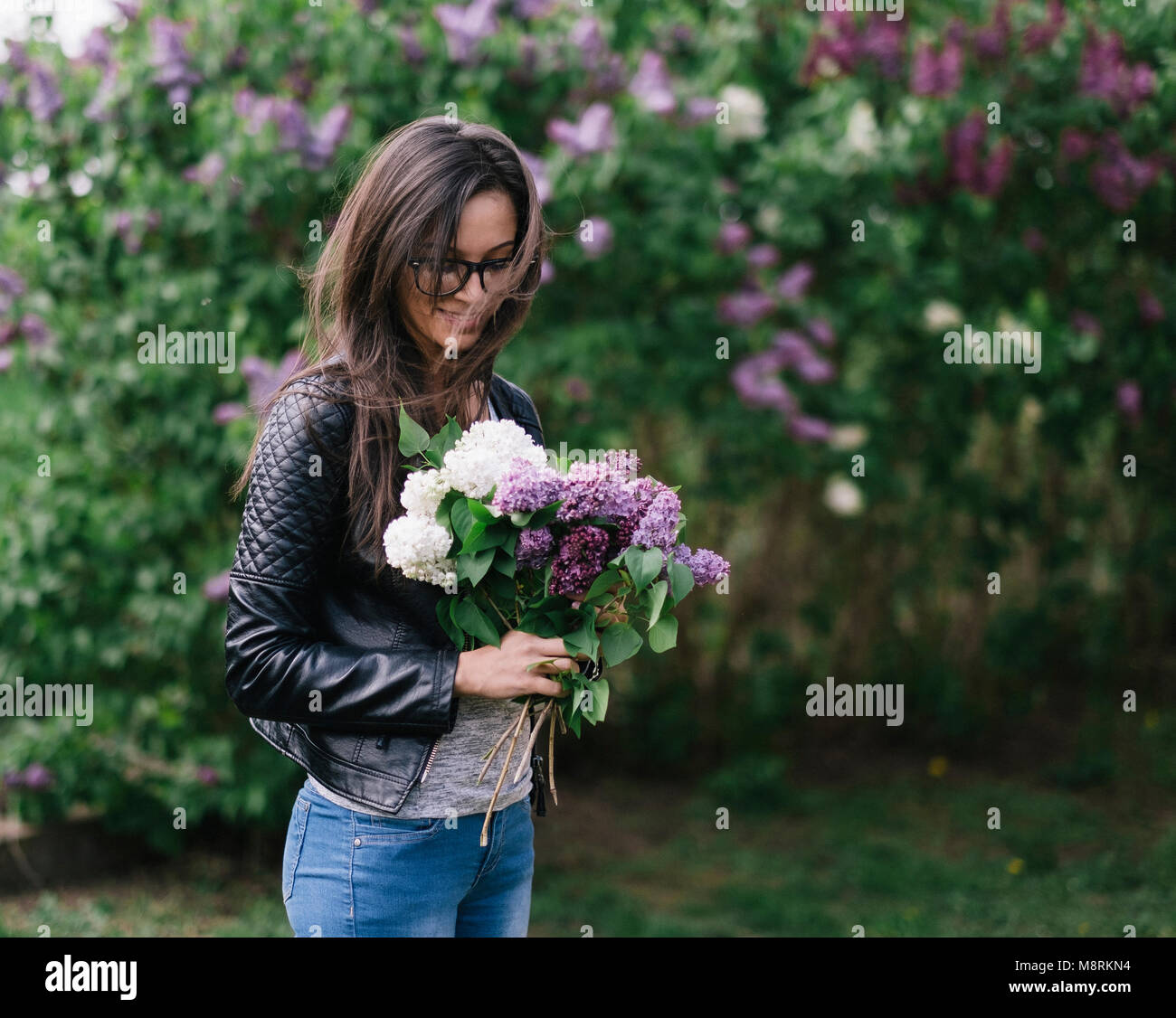 Junge Frau mit Blumen beim Stehen gegen blühende Pflanzen im Park Stockfoto