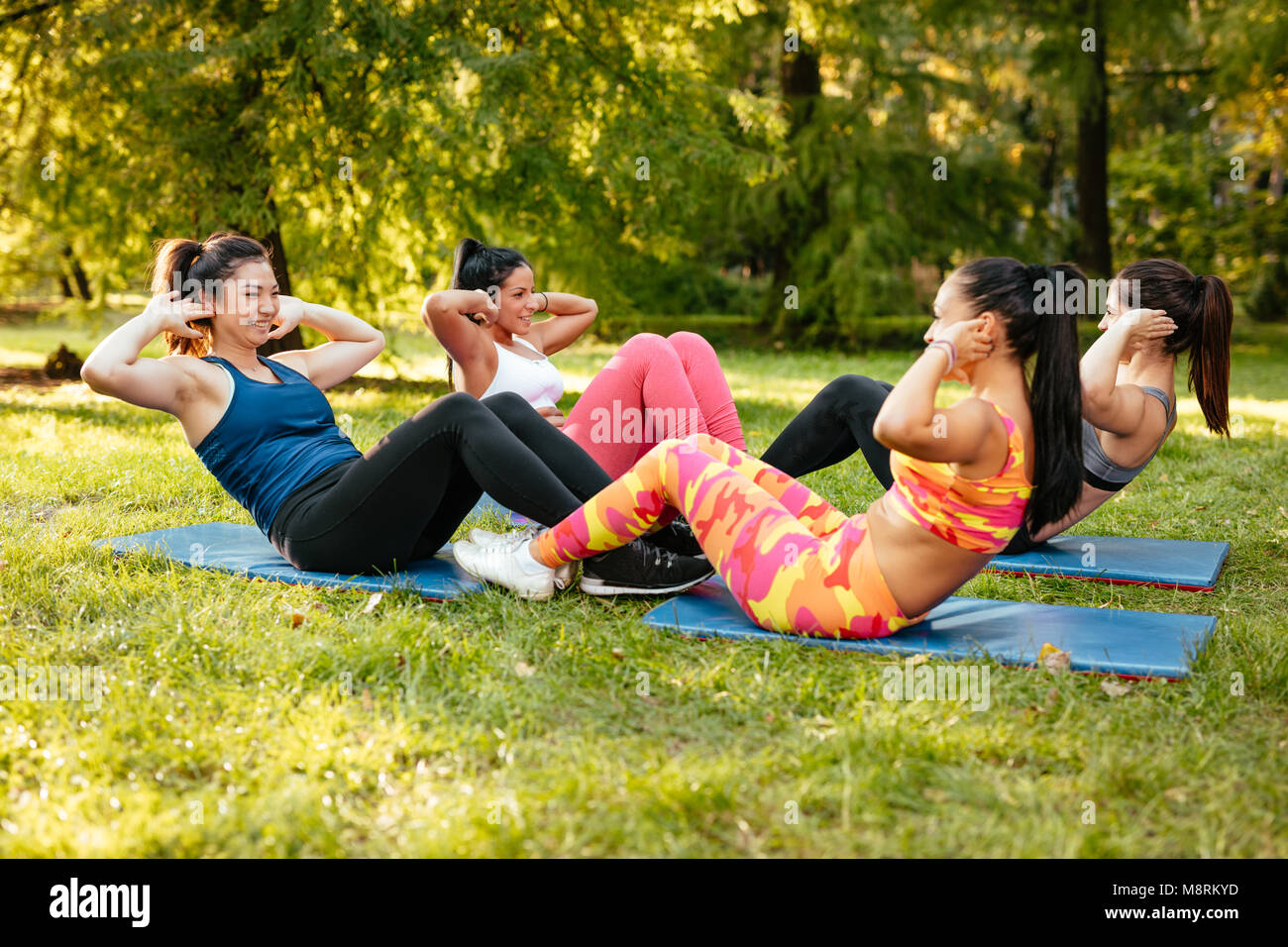 Vier schöne motivierte weibliche Freunde magen Übungen im City Park. Stockfoto