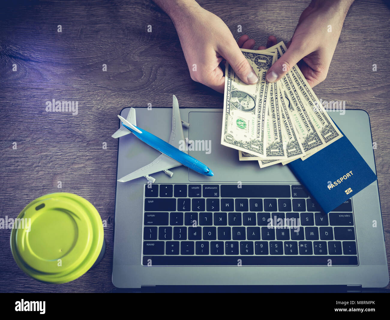 Die Hände des Mannes betrachten, Banknoten, die von einem Dollar, vor dem Hintergrund von einer Tasse Kaffee der Laptop, der Pass und das Flugzeug. Stockfoto