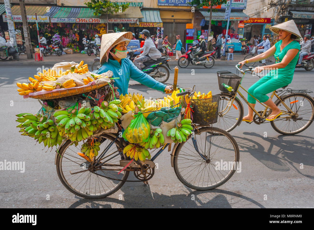 Vietnam Straße Frau, eine weibliche Verkäufer räder Fahrrad beladen mit Bananen entlang der Hauptstraße im Cholon Bereich von Saigon, Ho Chi Minh City, Vietnam Stockfoto