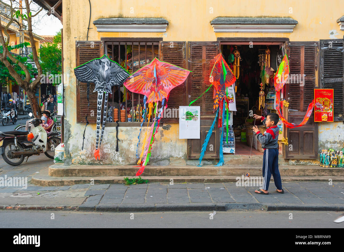 Vietnam Street Life, Blick auf ein vietnamesisches Kind, das mit einem Drachen vor einem farbenfrohen Drachenladen in der historischen Altstadt von Hoi an, Vietnam, spielt. Stockfoto