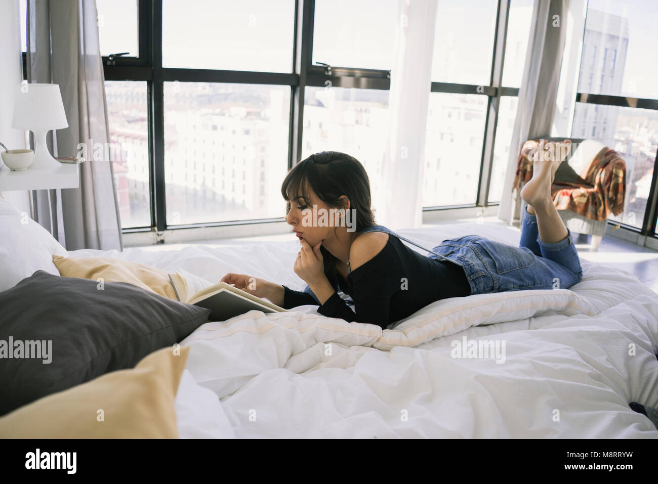 Die volle Länge der jungen Frau mit Buch beim liegen auf dem Bett zu Hause. Stockfoto