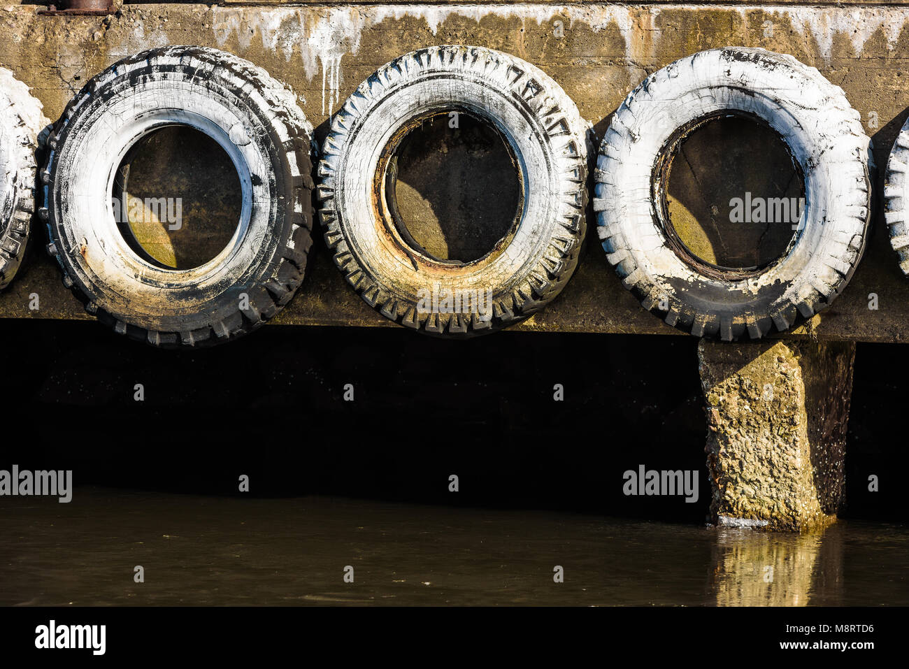 Drei weisse und verwitterten Autoreifen auf der Seite von einem Betonpfeiler in einem Hafen. Stockfoto