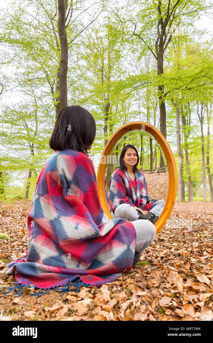 Kolumbianische Frau sitzt in Buchenwald mit Spiegel im Frühling Stockfoto