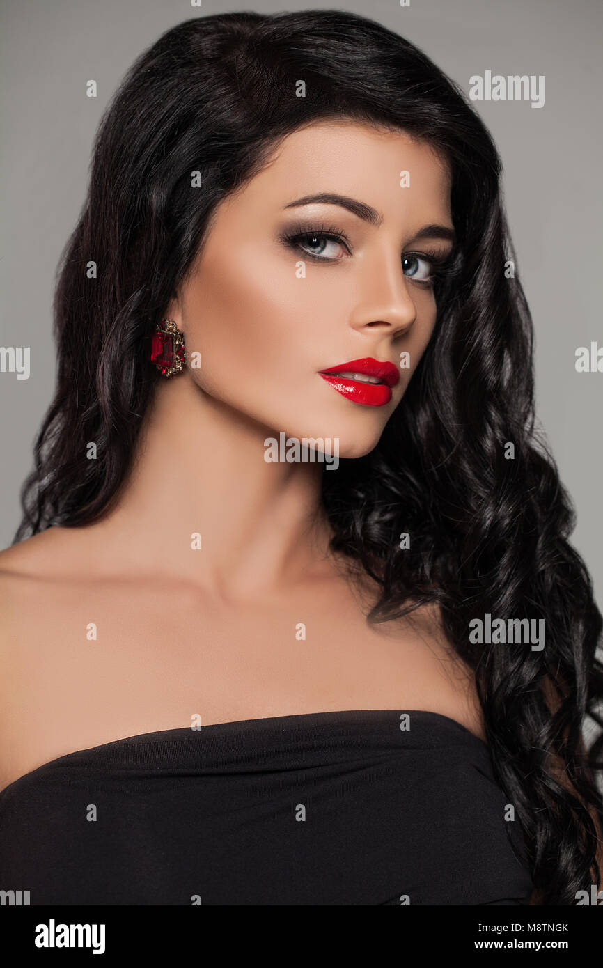 Perfekte Brunette Modell Gesicht. Junge Frau mit roten Lippen Make-up , Langes lockiges Haar und Rubin Ohrringe Stockfoto