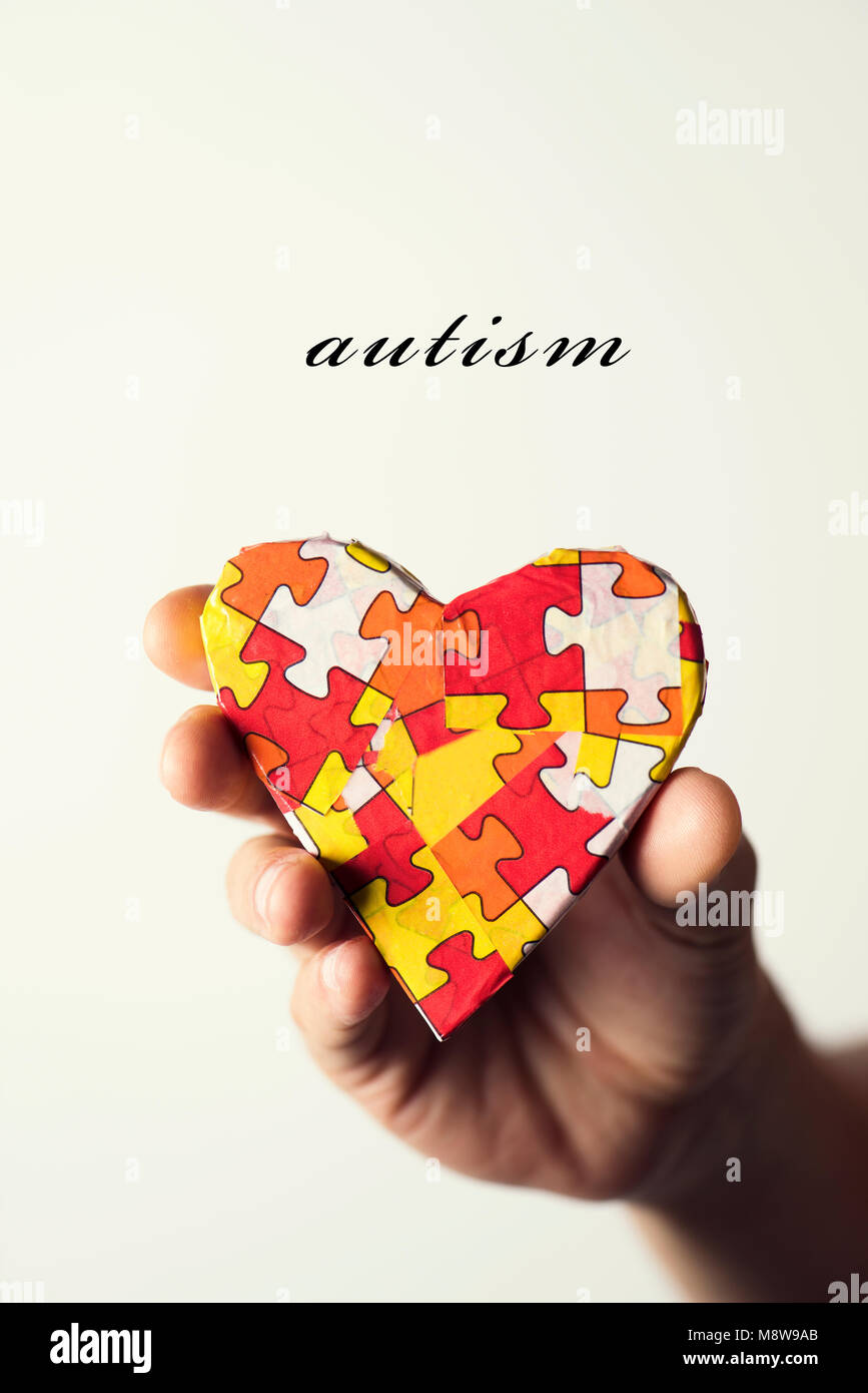 Das Wort Autismus und ein Herz mit vielen Puzzleteilen in verschiedenen Farben, Symbol der autism Bewußtsein, in der Hand des jungen kaukasischen ma gemusterten Stockfoto