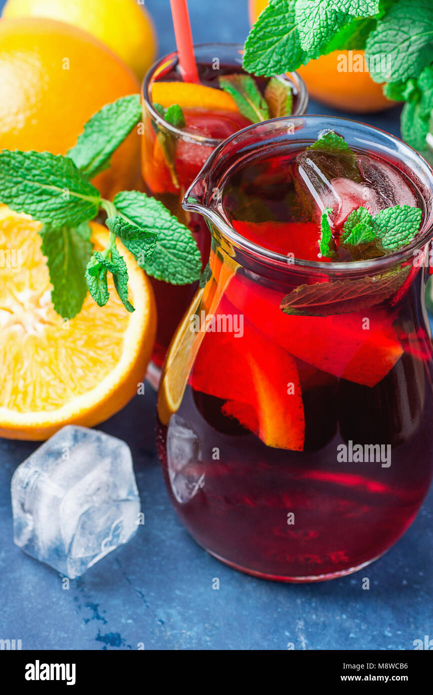 Erfrischende alkoholfreie Spanische Sangria aus der Vielfalt der Früchte Orange Citrus Granatapfel Trauben Beeren und frische Minze in Krug und Glas auf Blau B Stockfoto