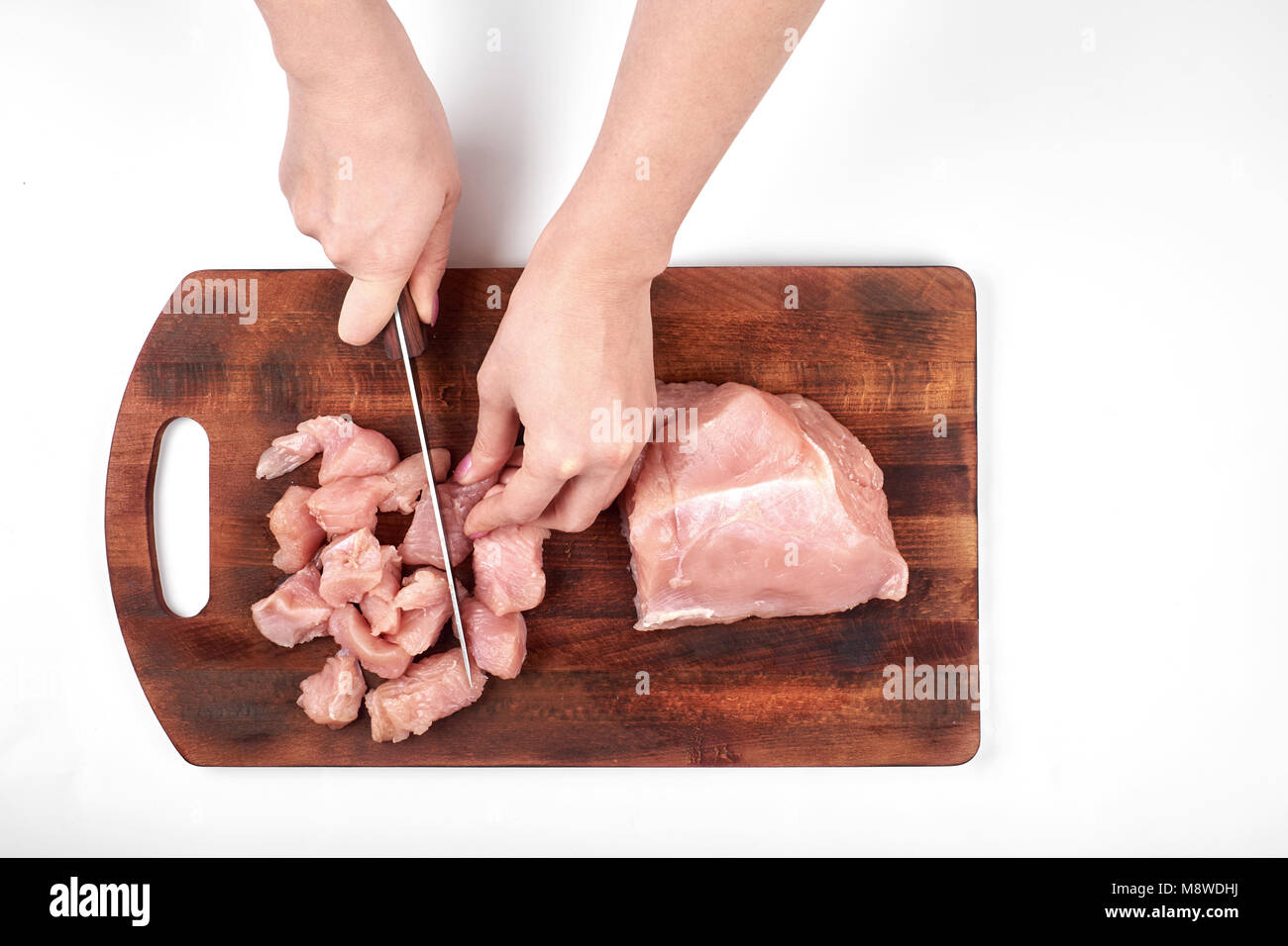 Schneiden von rohem Fleisch von Truthühnern mit einem Küchenmesser auf einem Schneidebrett auf weißem Hintergrund Stockfoto