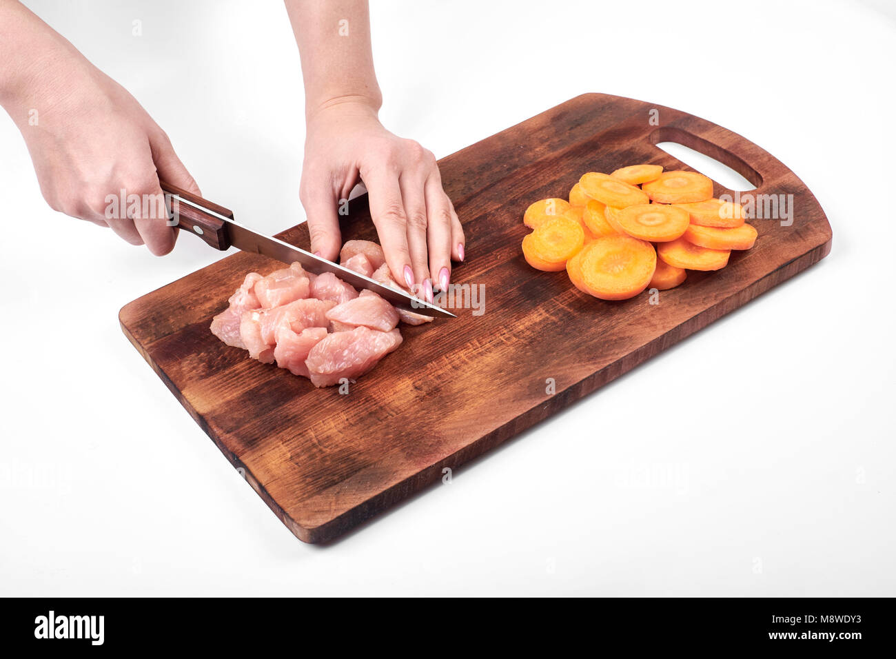 Schneiden von rohem Fleisch von Truthühnern und Karotte mit einem Küchenmesser auf einem Schneidebrett auf weißem Hintergrund Stockfoto