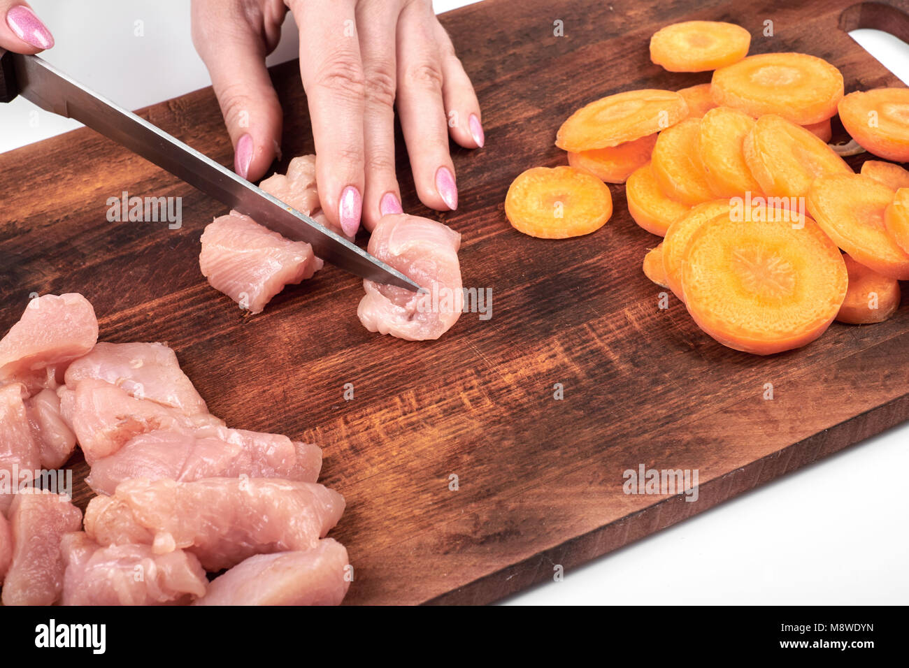 Schneiden von rohem Fleisch von Truthühnern und Karotte mit einem Küchenmesser auf einem Schneidebrett auf weißem Hintergrund Stockfoto