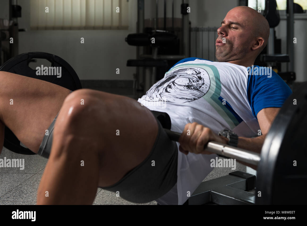 Starker Mann In der Turnhalle trainieren Kniesehnen mit Langhantel - Muskulös athletisch Bodybuilder Fitness Modell Übung Stockfoto
