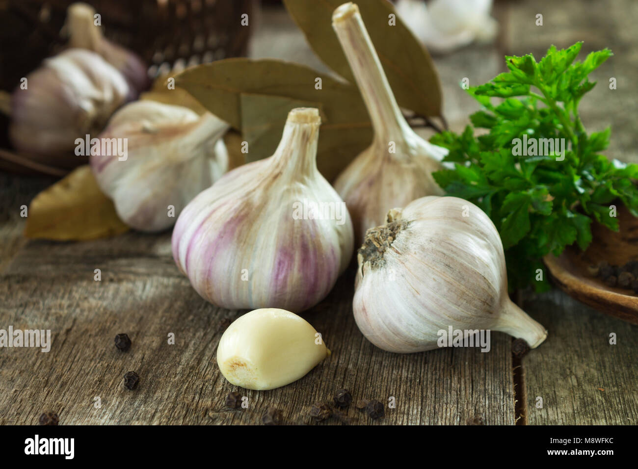 Gang und Knoblauch Köpfe close-up auf einen unscharfen Hintergrund aus Holz mit Petersilie und Lorbeerblätter. Flache Tiefenschärfe Stockfoto