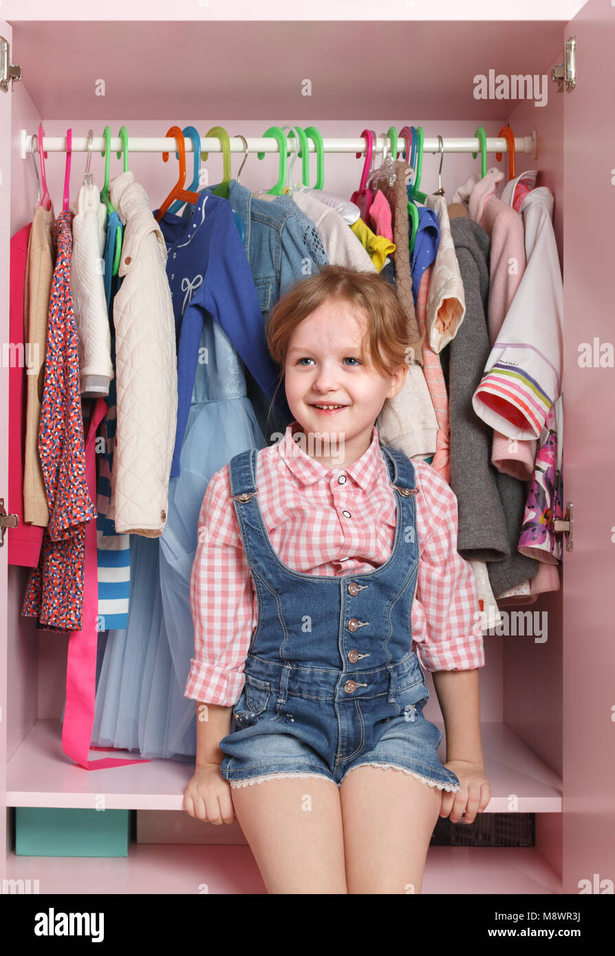 Ein kleines Mädchen sitzt in einem Schrank mit einer Abteilung. Storage System für Sachen für Kinder Stockfoto