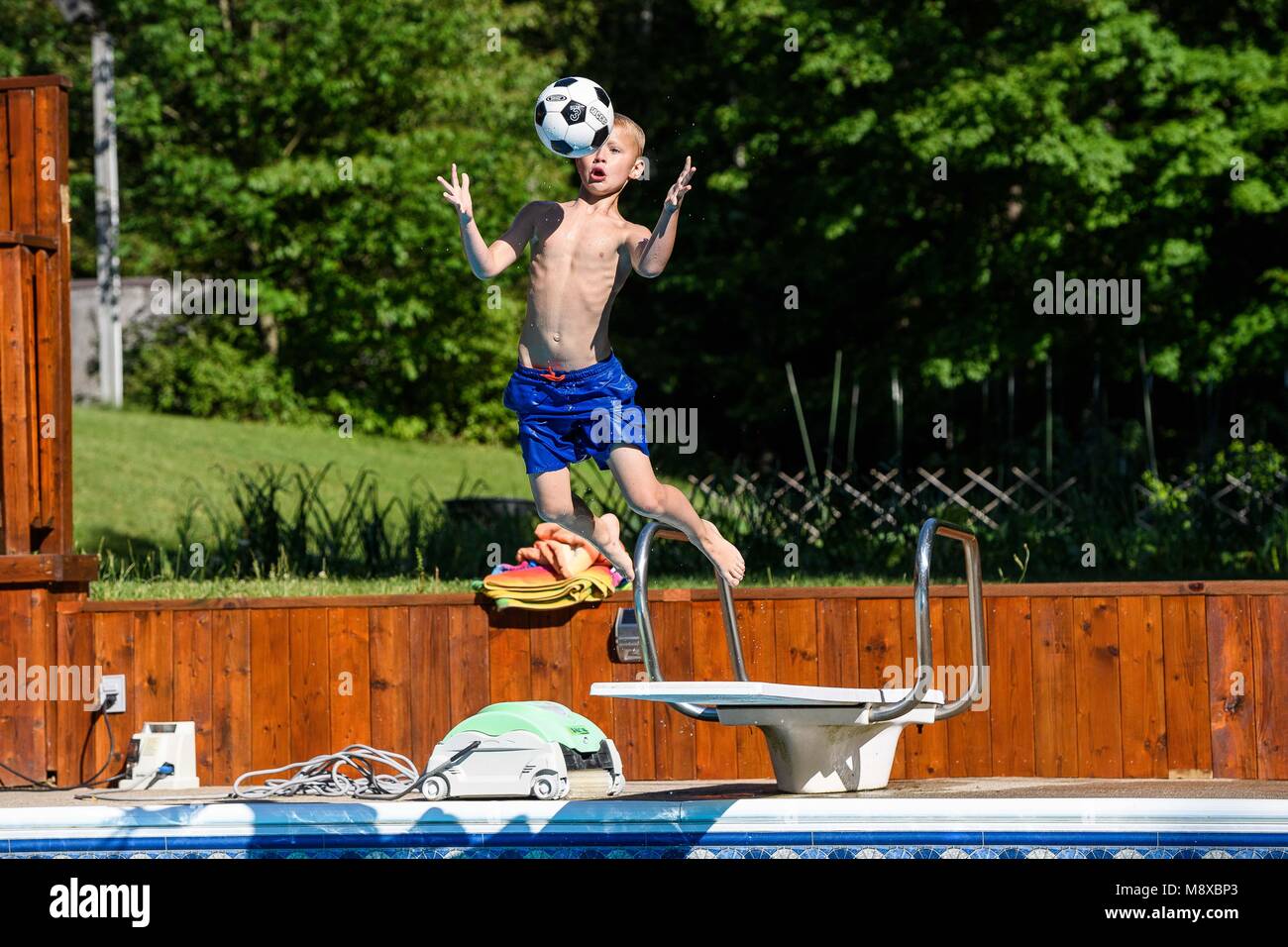 Junge beim Sprung in den Pool und fängt einen Ball Stockfoto