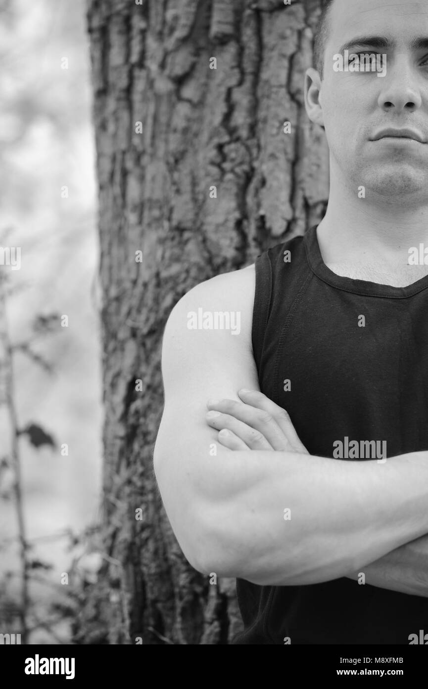Junger Mann muskulös Kreuzung Waffen im Wald Stockfoto