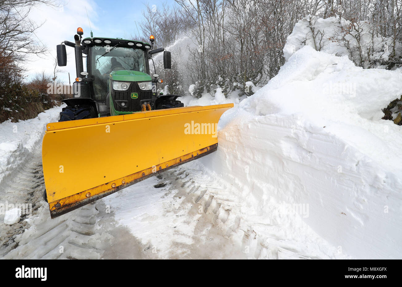 Ein Landwirt in einem Traktor hilft, den Schnee von einer blockierten Straße zu räumen, die aus Simonsbath im Exmoor Nationalpark führt, Da die eisigen Bedingungen, die von der 'Mini Beast aus dem Osten' gebracht werden, noch einen Tag anhaften werden, bevor Großbritannien die Rückkehr des Frühlings sehen wird. Stockfoto