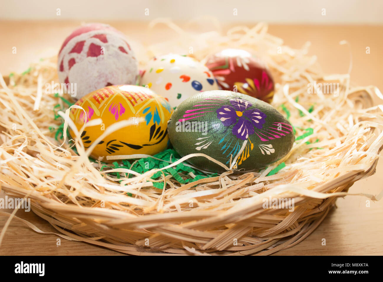 Im Weidenkorb auf dem hölzernen Tisch sind einem bunten Ostereier. Stockfoto