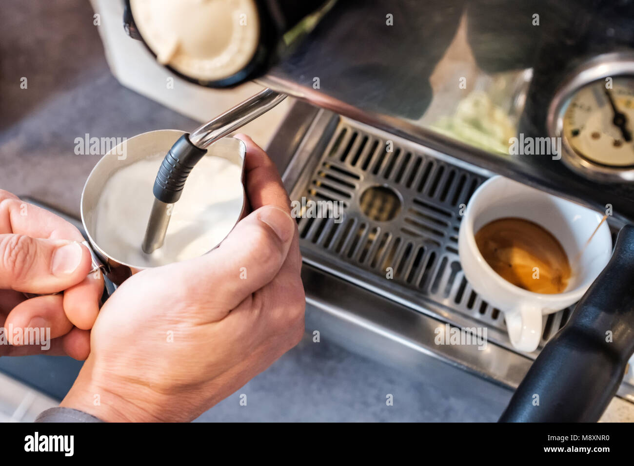 Barista dämpfen und Aufschäumen der Milch in Edelstahl Zuhaltung mit Espresso maching für Cappuccino oder Latte Stockfoto