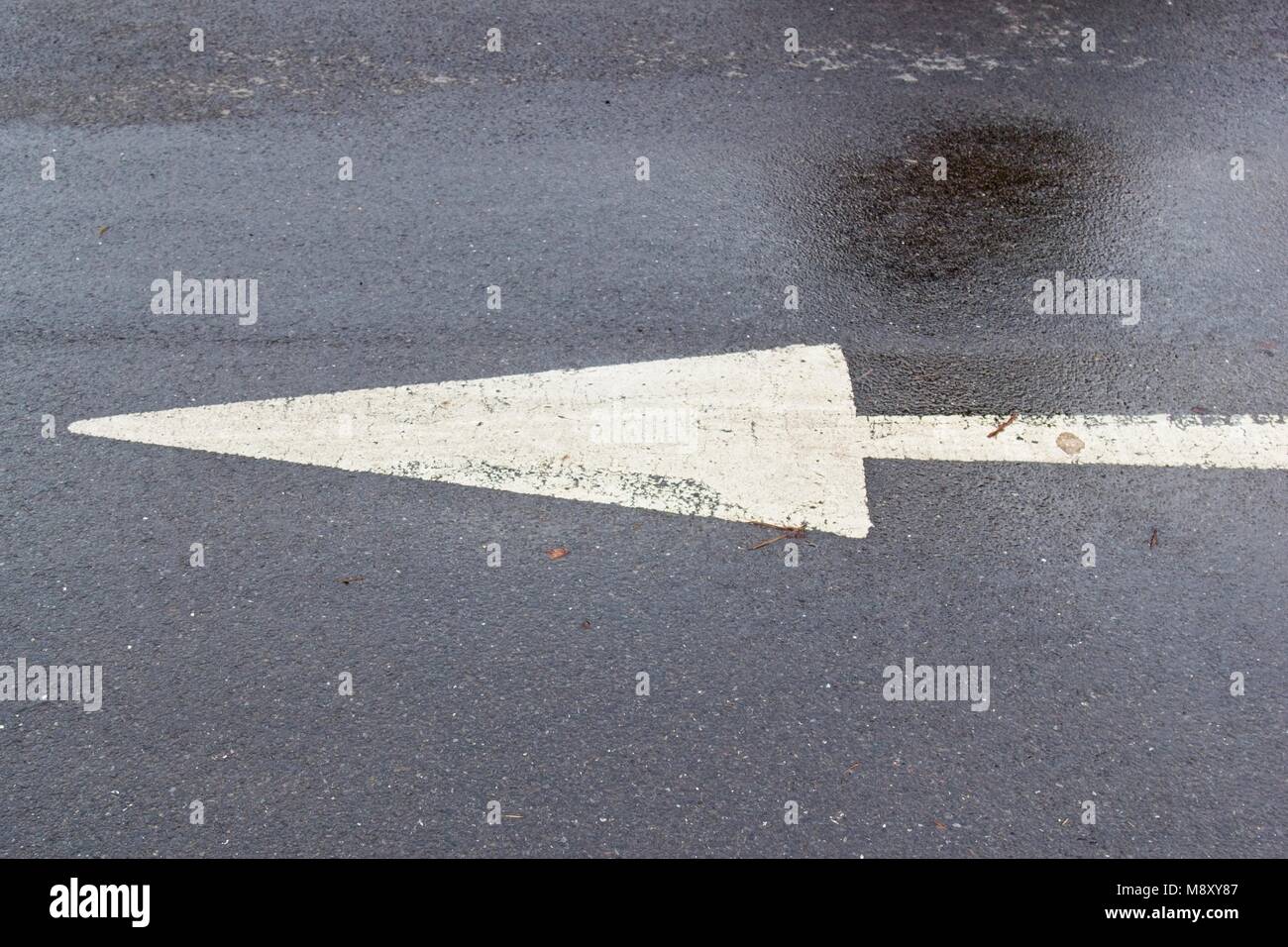 Weiß lackierten Pfeil nach links Kennzeichnung auf dunklen nassen Straße Stockfoto