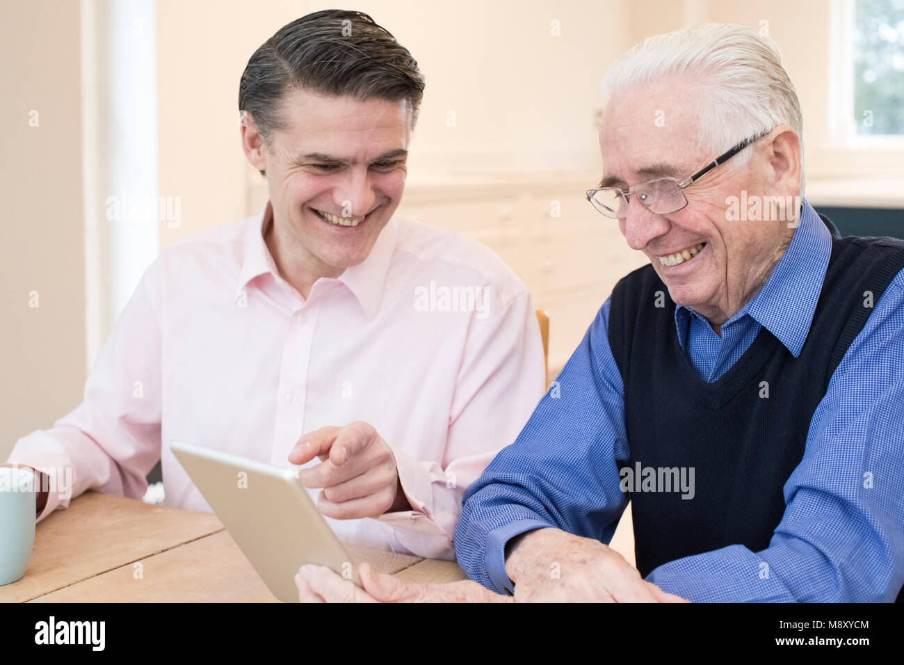 Männliche Nachbar Zeigt älteren Menschen, wie Sie mit digitalen Tablet Stockfoto