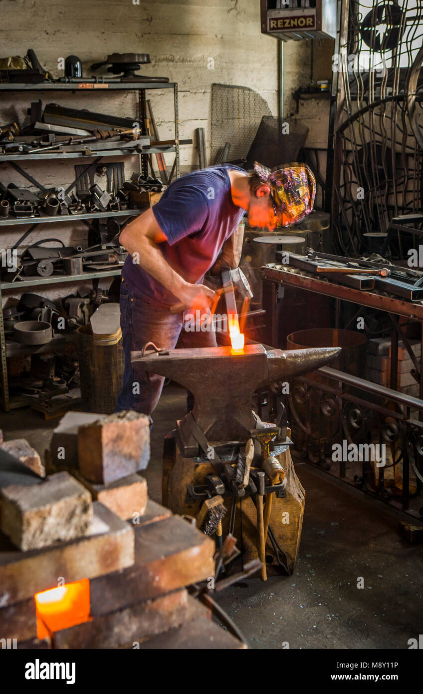 Ein Mann in einem Schmied Workshop mit Hammer und Amboss arbeiten. Stockfoto