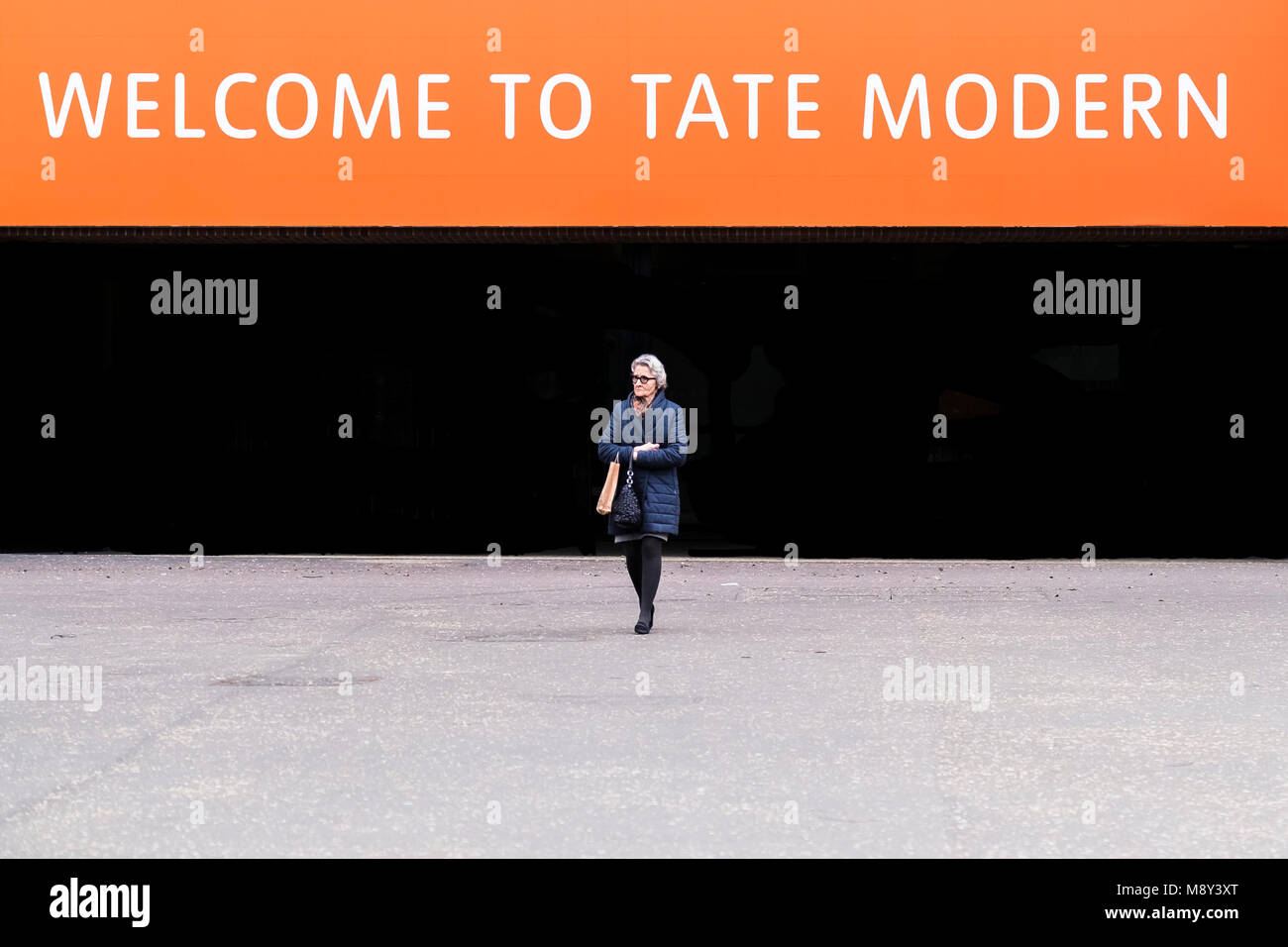 Eine reife Frau vor ein willkommenes Zeichen über einen Eingang zu Tate Modern auf der South Bank in London. Stockfoto
