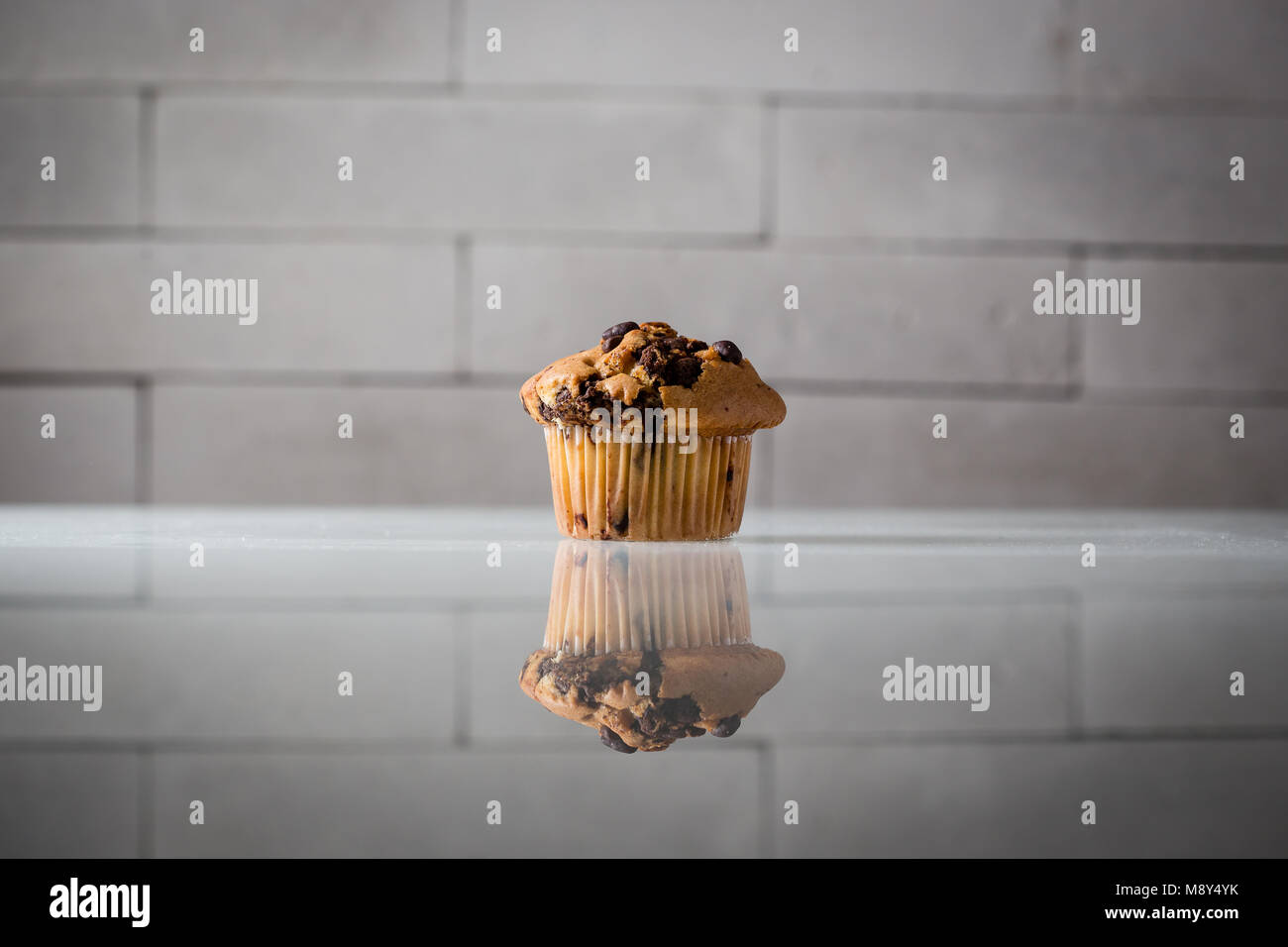 Chocolate Chip Muffin oder Cupcake auf Glas Tisch, grau Ziegelstein Hintergrund, Beleuchtung, Produktfotografie, harte Schatten Stockfoto