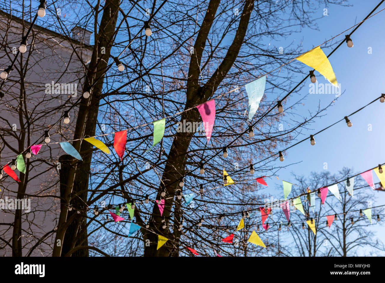 Bunte dreieckige Fahnen flattern auf Äste vor blauem Frühlingshimmel. Deko für die Party im Freien. Stockfoto