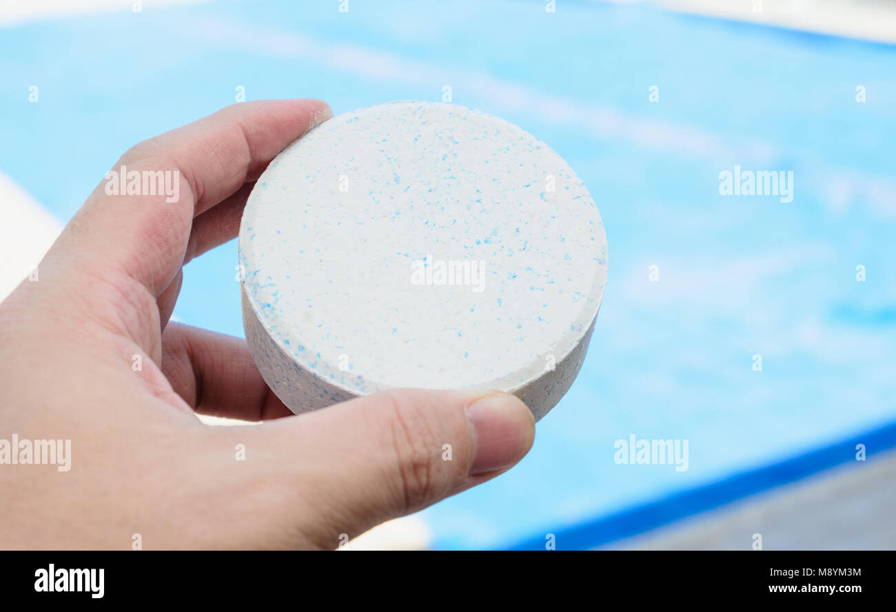 Hand mit einem weißen gerundeten Chlortablette. Unfocused Swimmingpool auf dem Hintergrund. Stockfoto