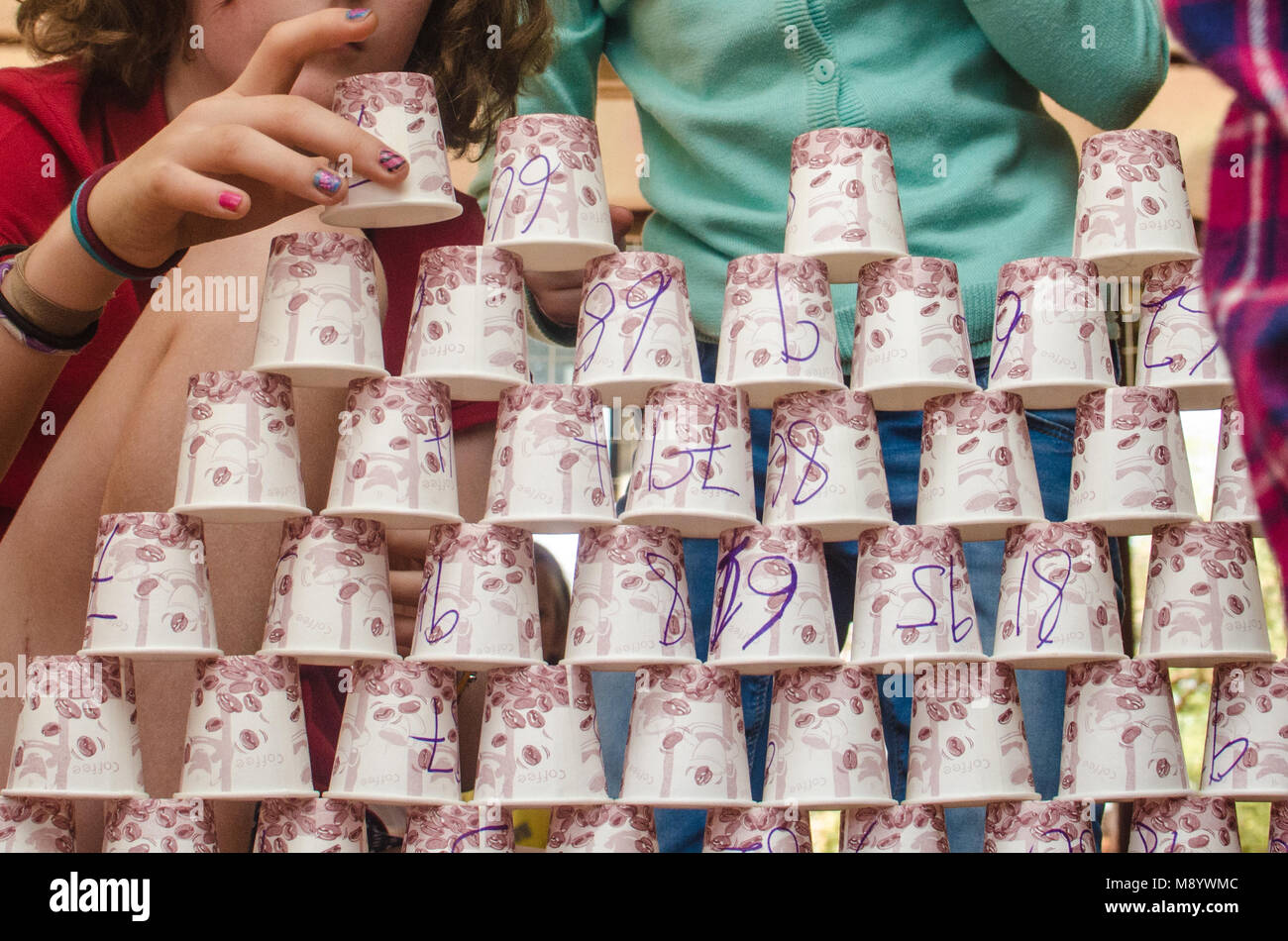 Ein Mädchen setzt einen Pappbecher auf ihr Papier cup Tower. Sie und andere Kinder können Arbeiten an der Schule Projekt gesehen werden. Stockfoto